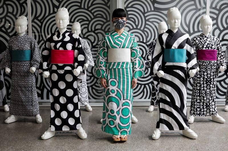 &copy; Reuters. Japanese artist Hiroko Takahashi wears a protective face mask as she poses for a photograph in front of mannequins displaying yukata, a lighter kimono which she designed, at her studio in Tokyo