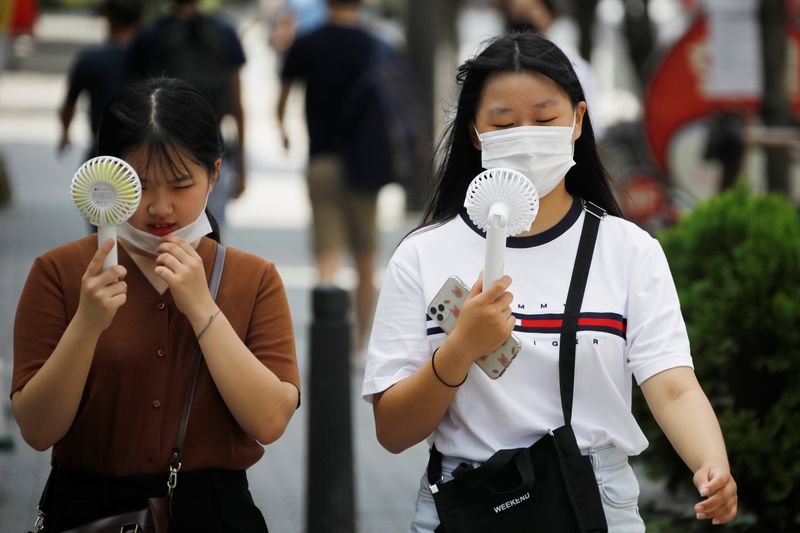 © Reuters. Women wearing masks to prevent the spread of the coronavirus disease (COVID-19) use portable fans to cool down in Seoul