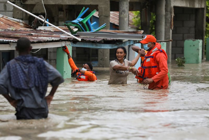 © Reuters. Members of the Civil Defence help a woman in a flooded street after the passage of Storm Laura, in Azua