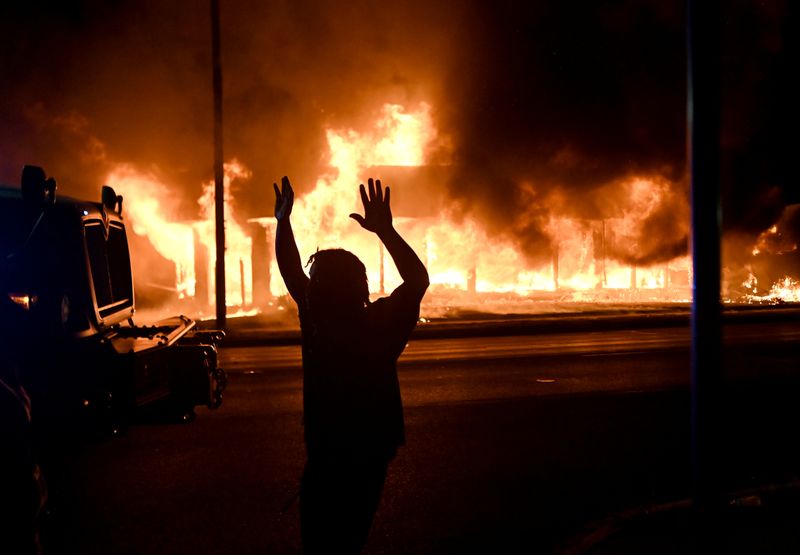 &copy; Reuters. Un hombre camina al lado de un vehículo blindado mientras B&amp;L Office Furniture se quema en el fondo después de protestas que terminaron en incendios luego de que la policía disparó varias veces a un hombre negro, identificado como Jacob Blake, ano