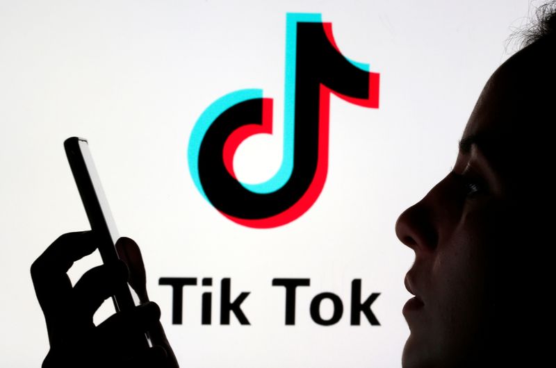 &copy; Reuters. A person holds a smartphone as Tik Tok logo is displayed behind in this picture illustration