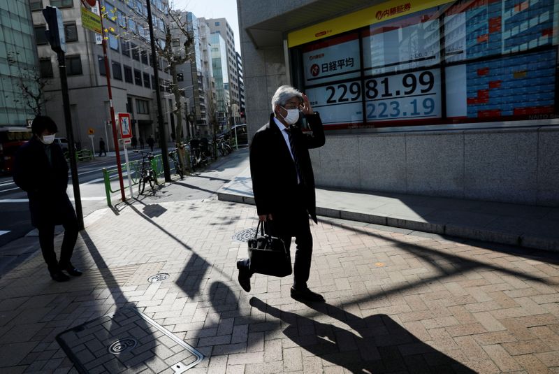 &copy; Reuters. People wearing surgical masks walk past a screen showing Nikkei index outside a brokerage in Tokyo