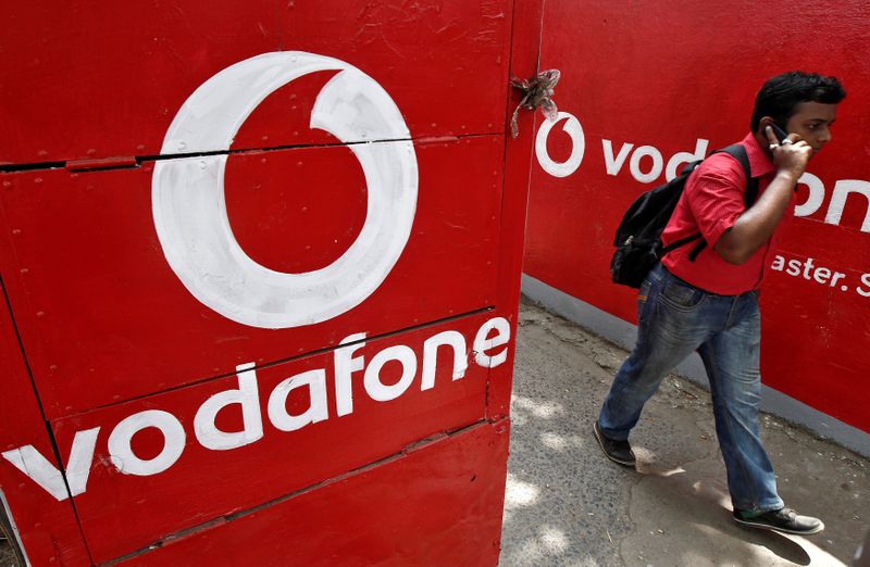 &copy; Reuters. Man speaks on his mobile phone as he walks past the logos of Vodafone painted on a roadside wall in Kolkata
