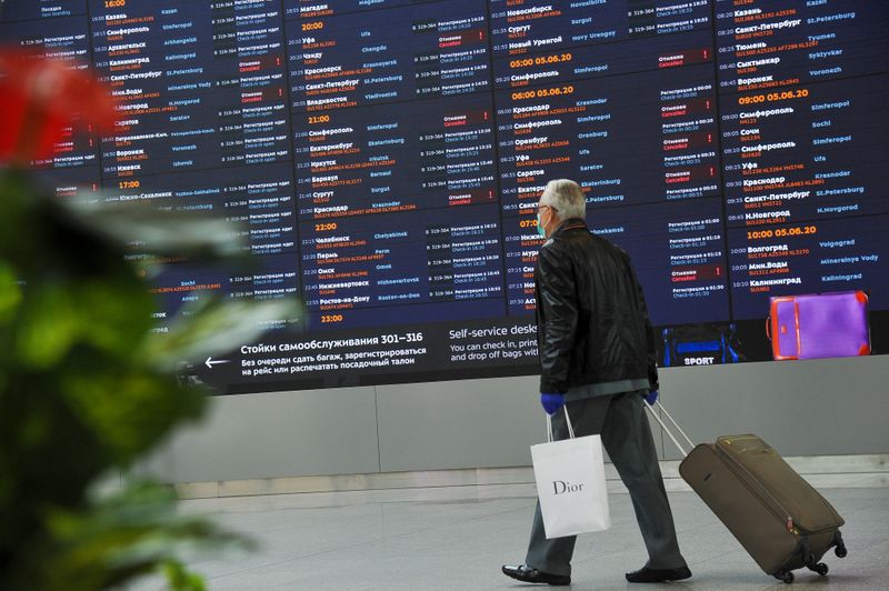 &copy; Reuters. A passenger wearing a protective face mask and gloves walks past a departures board at Sheremetyevo International Airport outside Moscow