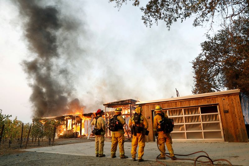 &copy; Reuters. FILE PHOTO: A group of firefighters look on as a house burns during the wind-driven Kincade Fire in Healdsburg, California