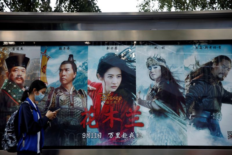 &copy; Reuters. Женщина проходит мимо рекламы фильма &quot;Мулан&quot; компании Walt Disney на автобусной остановке в Пекине