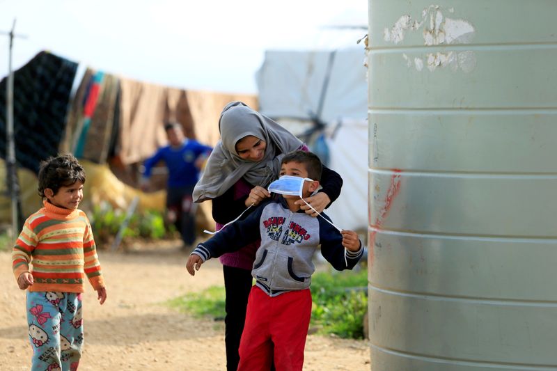 © Reuters. FILE PHOTO: A Syrian refugee woman puts a face mask on a boy as a precaution against the spread of coronavirus, in al-Wazzani area in southern Lebanon