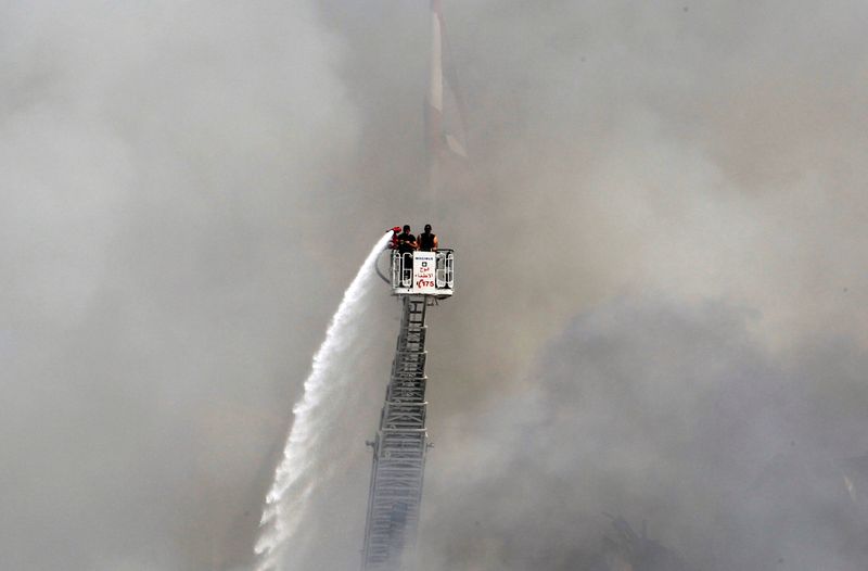 © Reuters. A man uses a water hose to put out the remains of a fire that broke out at Beirut's port yesterday