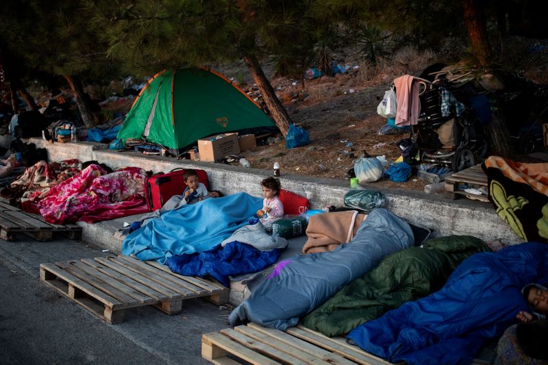 &copy; Reuters. FILE PHOTO: Two children eat cookies as refugees and migrants from the destroyed Moria camp sleep on the side of a road, on the island of Lesbos