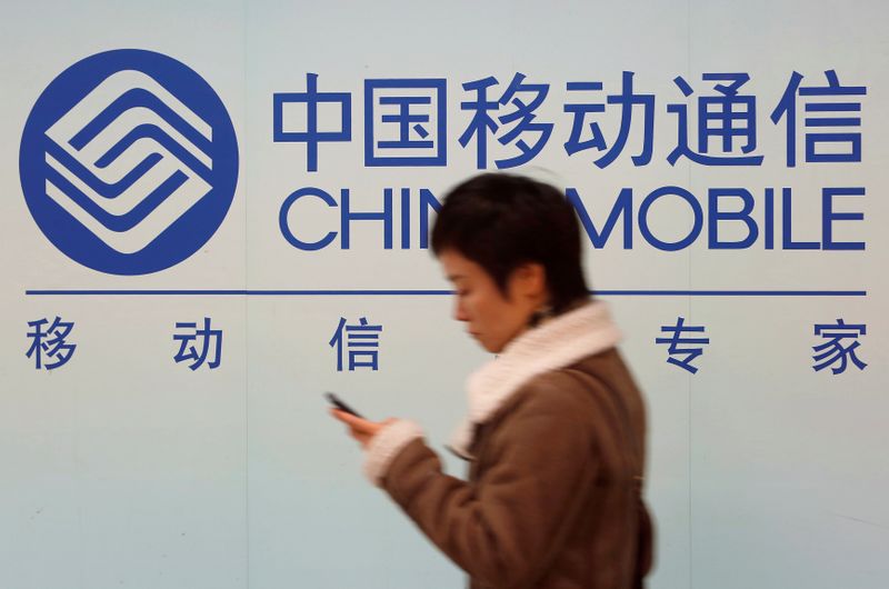 © Reuters. FILE PHOTO: A woman looks at the screen of her mobile phone while walking past a China Mobile sign in downtown Shanghai