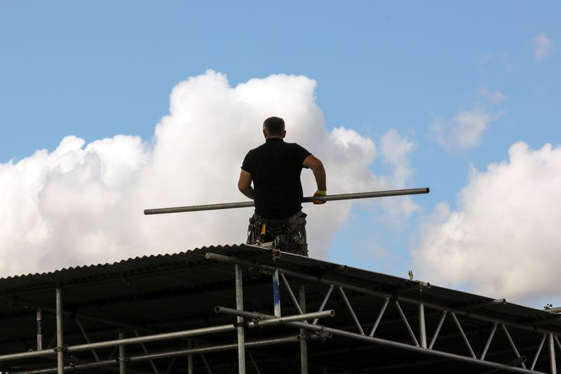 © Reuters. FILE PHOTO: A construction worker carries a scaffold pole on the roof of a house in London