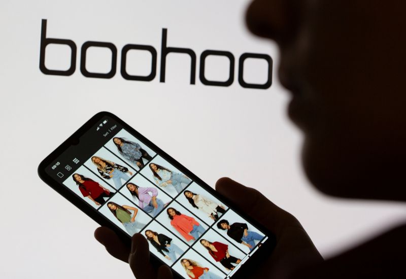 © Reuters. A woman poses with a smartphone showing the Boohoo app in front of the Boohoo logo on display in this illustration