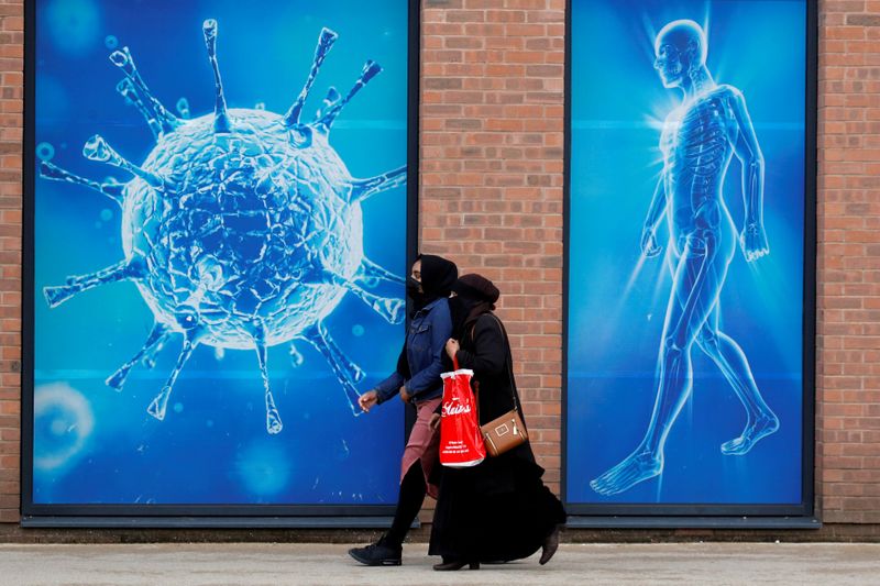 &copy; Reuters. FOTO DE ARCHIVO: Dos personas caminan frente a una ilustración de un virus en Oldham