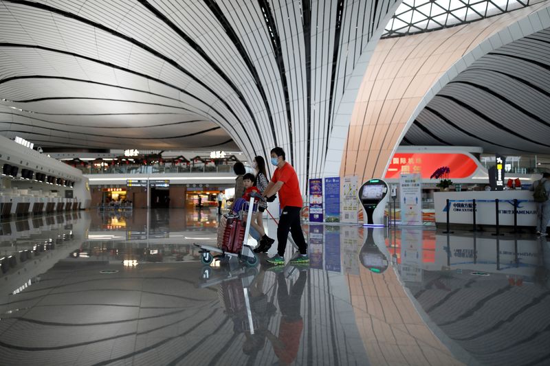 © Reuters. FILE PHOTO: Passengers wearing face masks following the coronavirus disease (COVID-19) outbreak walk with luggages at a terminal hall of the Beijing Daxing International Airport ahead of Chinese National Day holiday, in Beijing