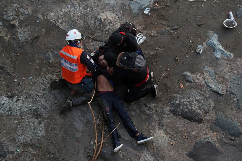 &copy; Reuters. MATERIAL SENSIBLE. Foto del viernes de personal de asistencia dando primeros auxilios a un manifestante que cayó de un puente durante una protesta en el centro de Santiago