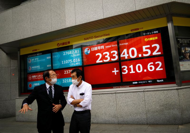 &copy; Reuters. Men wearing protective face masks chat in front of a screen displaying Nikkei share average and world stock indexes, amid the coronavirus disease (COVID-19) outbreak, in Tokyo
