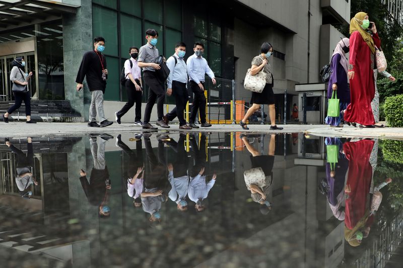&copy; Reuters. People wearing protective masks are reflected in a water puddle as they cross a street, amid the coronavirus disease (COVID-19) outbreak in Kuala Lumpur