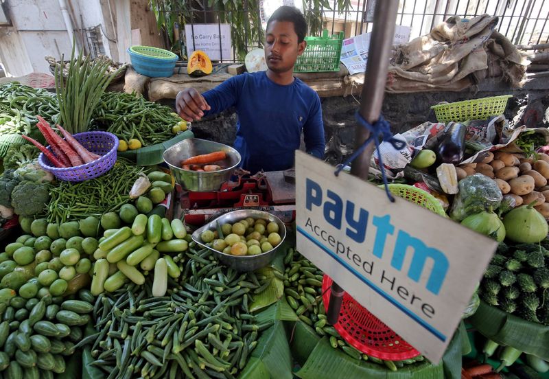 &copy; Reuters. FILE PHOTO: A vendor weighs vegetable next to an advertisement of Paytm, a digital payments firm, hanging amidst his vegetables at a roadside market in Mumbai