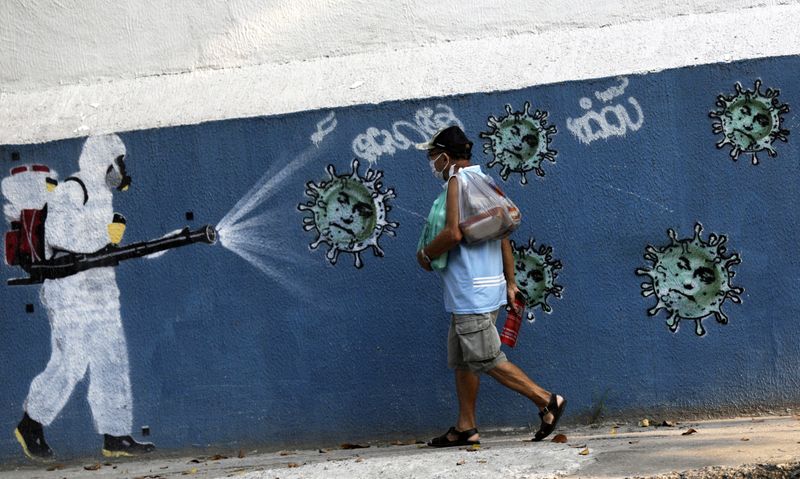 &copy; Reuters. Un hombre camina junto a un grafiti que muestra a un limpiador con equipo de protección rociando virus con la cara del presidente de Brasil Jair Bolsonaro, en medio del brote de la enfermedad coronavirus (COVID-19), en Río de Janeiro, Brasil.
