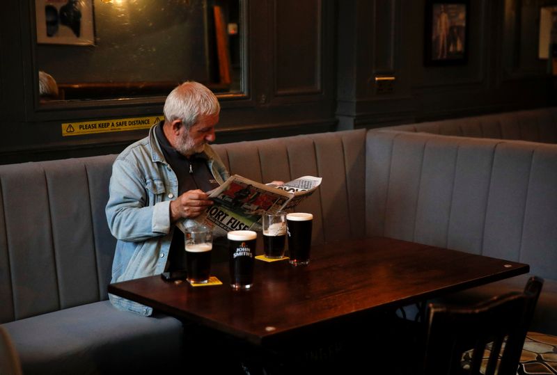 &copy; Reuters. A man reads a newspaper as he sits inside the Grapes pub in Liverpool