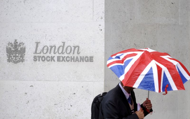 &copy; Reuters. Un uomo con un ombrello cammina davanti al logo London Stock Exchange nella City londinese