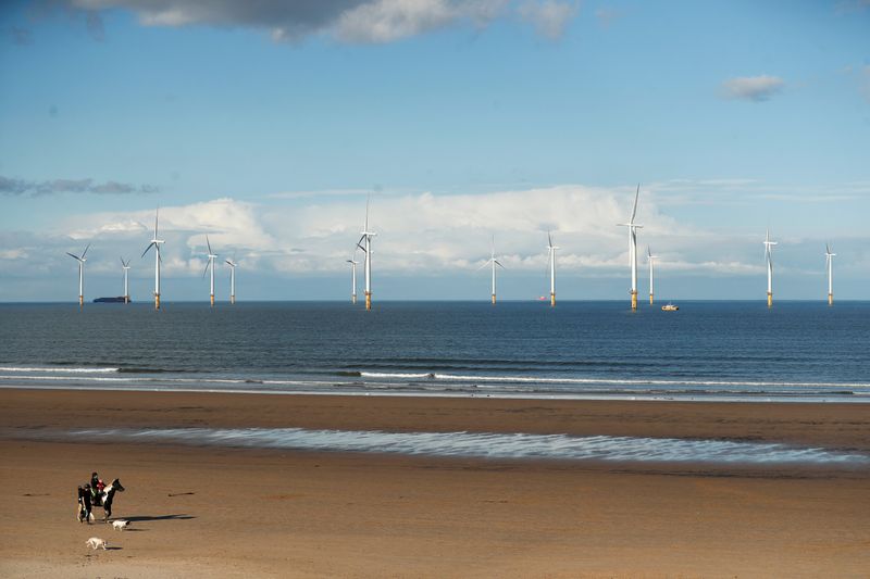 © Reuters. Wind turbines are seen in the background as people stroll along Redcar Beach in Redcar