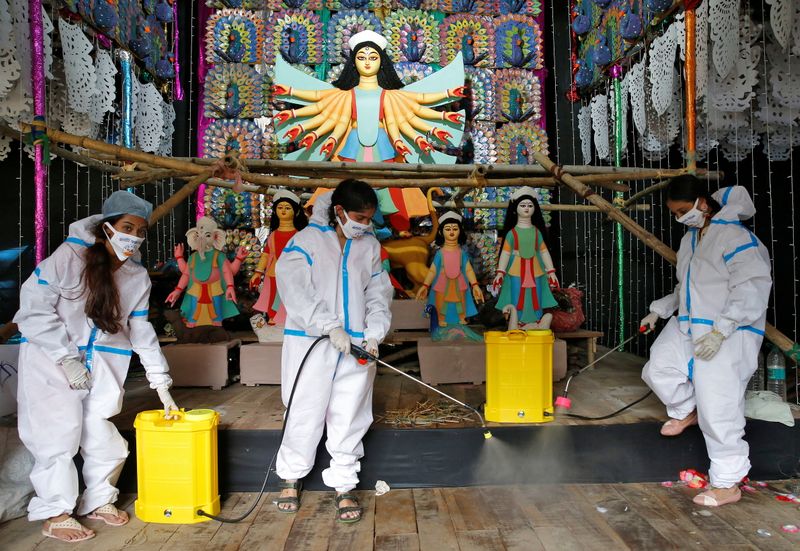 &copy; Reuters. Women wearing personal protective equipment sanitize a &quot;pandal&quot; ahead of Durga Puja festival in Kolkata