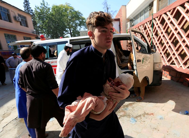 © Reuters. FILE PHOTO: A man carries an injured child at a hospital after a truck bomb blast, in Jalalabad