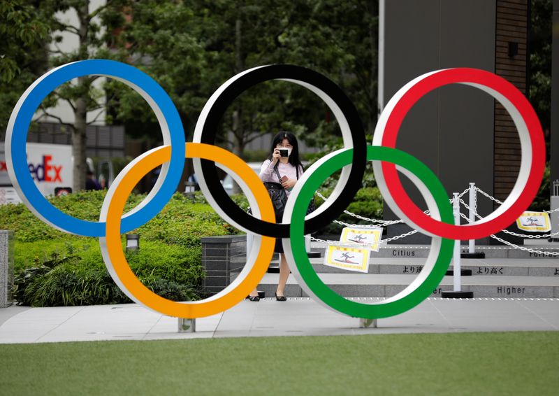 © Reuters. A woman wearing a protective mask amid the coronavirus disease (COVID-19) outbreak, takes a picture of the Olympic rings in front of the National Stadium in Tokyo