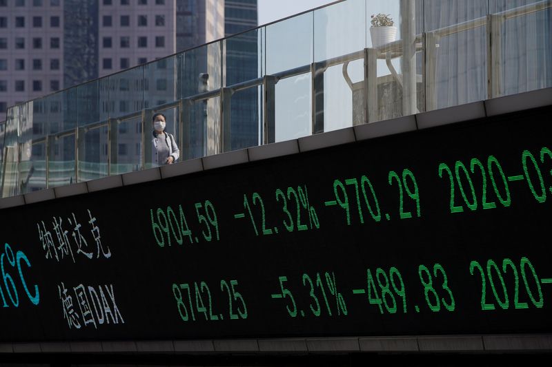 &copy; Reuters. Un passante su un un ponte con informazioni sugli indici della Borsa di Shanghai