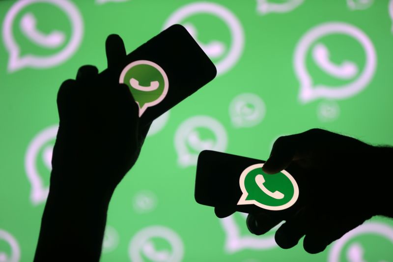 © Reuters. Men pose with smartphones in front of displayed Whatsapp logo in this illustration