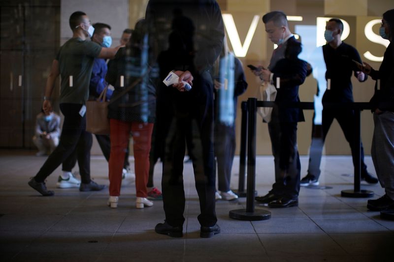 &copy; Reuters. A staff member holds a thermometer as people wait at an Apple Store before Apple&apos;s 5G new iPhone 12 go on sale, as the coronavirus disease (COVID-19) outbreak continues in Shanghai