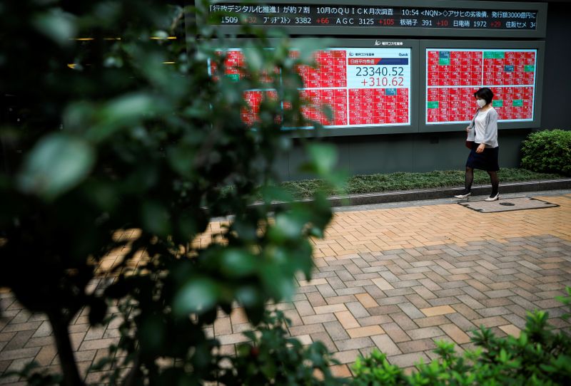 &copy; Reuters. Una donna con una mascherina passa davanti a uno schermo con dati sulla Borsa di Tokyo