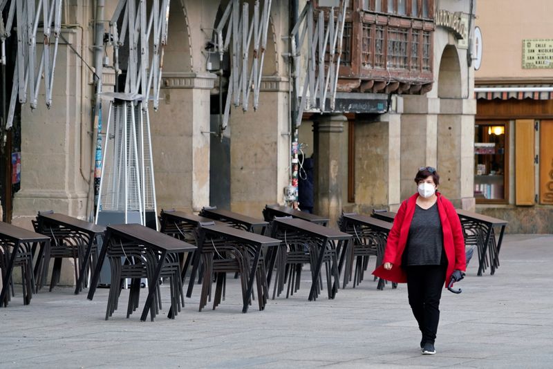 &copy; Reuters. Una mujer con mascarilla camina frente a la terraza de un bar cerrado en Pamplona