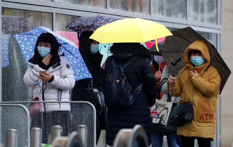 &copy; Reuters. FILE PHOTO: People wearing face masks shelter under umbrellas outside a department store following the outbreak of the coronavirus disease (COVID-19) in Manchester