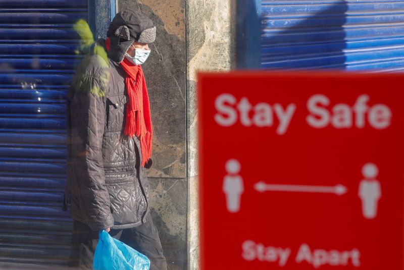 &copy; Reuters. Pessoa com máscara de proteção perto de placa que sinaliza distanciamento social em Coventry, no Reino Unido
