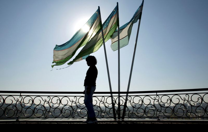 &copy; Reuters. A girl is silhouetted against sun standing next to Uzbek flags in Tashkent