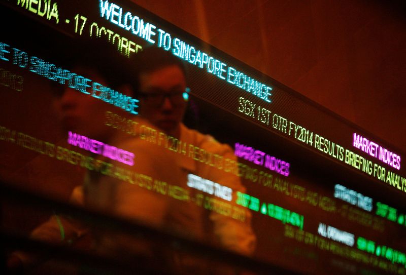 © Reuters. FILE PHOTO: People pass stock index tickers at the Singapore Exchange (SGX) premises