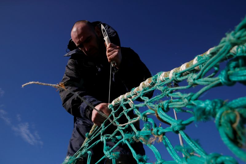 &copy; Reuters. A fisherman repairs a fishing net on the dock of the port in Boulogne-sur-Mer