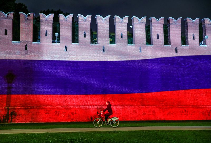 &copy; Reuters. A woman rides a bicycle past a part of the Kremlin wall where the Russian national flag is projected, during celebrations of Russia Day in Moscow