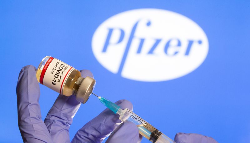 &copy; Reuters. Mulher segura frasco rotulado como de vacina contra Covid-19 em frente a logo da Pfizer em foto de ilustração
