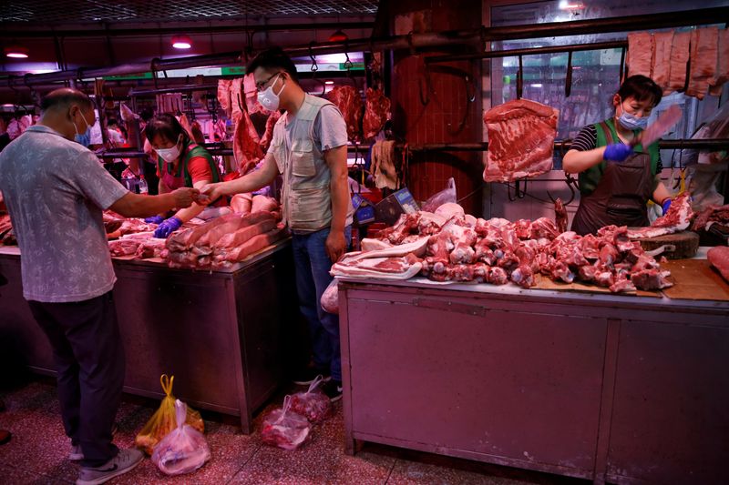 © Reuters. customer wearing a face mask pays for pork as a vendor chops pork meat inside the Yuegezhuang wholesale market, following new cases of coronavirus disease (COVID-19) infections in Beijing
