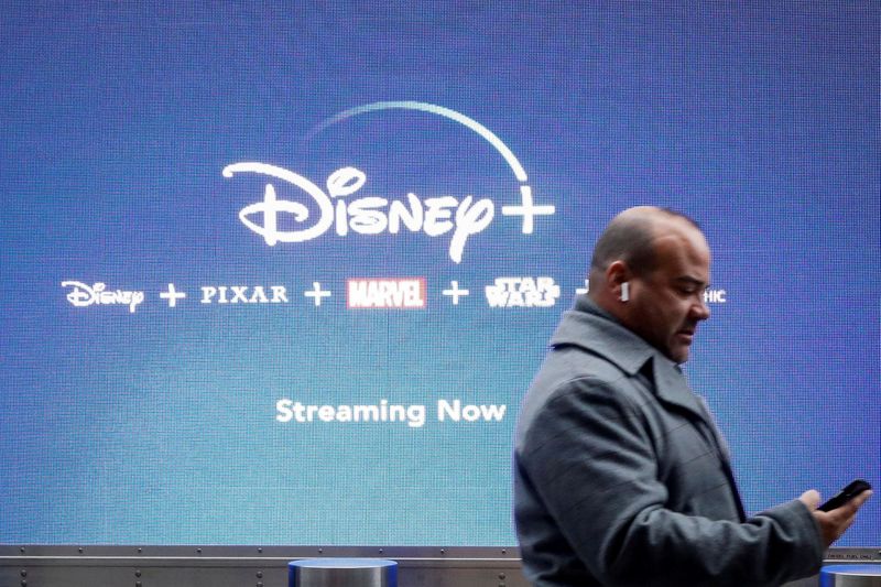 © Reuters. FILE PHOTO: A man looks at his phone as he passes by a screen advertising Walt Disney's streaming service Disney+ in New York