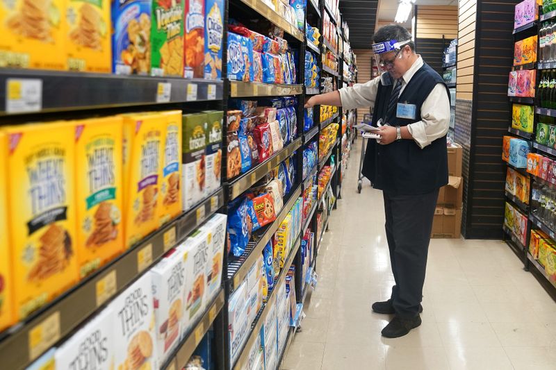 © Reuters. FILE PHOTO: A worker with a face shield checks products on the shelf of a grocery store