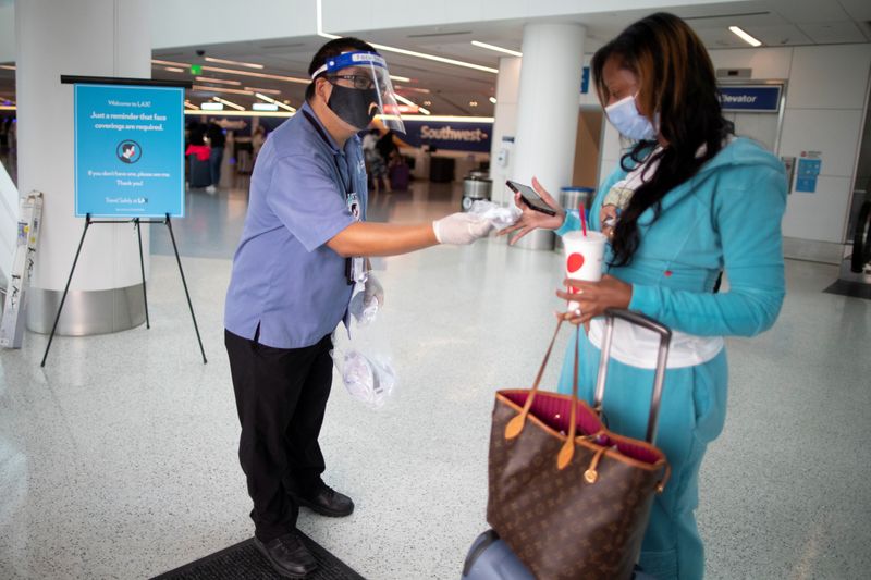 &copy; Reuters. Travel Safely Ambassador Carlos Hernandez hands out a face masks to an airline passenger at LAX airport, as the global outbreak of the coronavirus disease (COVID-19) continues, in Los Angeles