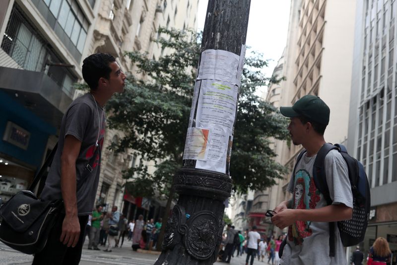 © Reuters. FILE PHOTO: Young men look at job listings posted on a street in Sao Paulo