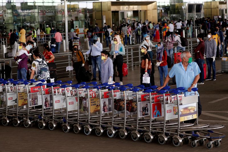 © Reuters. FILE PHOTO: An airport staff member pushes trolleys at Mumbai's airport after the Indian government allowed domestic flight services to resume