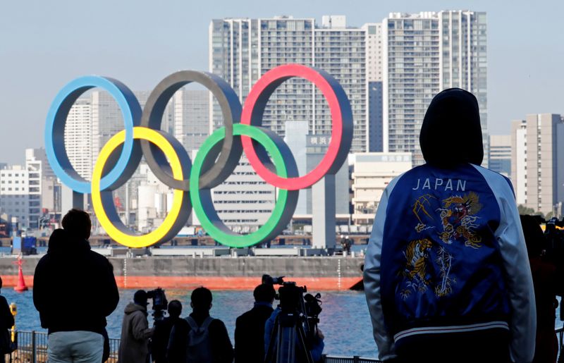 &copy; Reuters. Dei passanti osservano la scultura degli anelli olimpici, riposizionata nella zona del parco marino di Odaiba dopo essere stata rimossa per operazioni di manutenzioni durante la pandemia di coronavirus a Tokyo