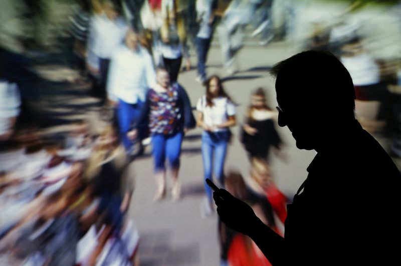 &copy; Reuters. FILE PHOTO: A man looks at data on his mobile as background with crowd of people walking is projected in this picture illustration