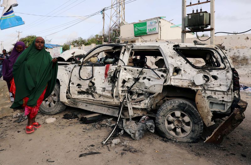 © Reuters. FILE PHOTO: Somali women walk near the wreckage of a car destroyed at the scene of a militant attack at the Elite Hotel in Lido beach, in Mogadishu